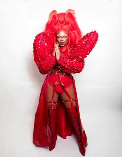 Aimee Yonce Shennel wearing a red strappy bodysuit with dramatic sleeves and matching cape.