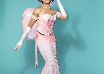 Pepper posing happily wearing a light pink form-fitting gown with large back bow and matching opera gloves.