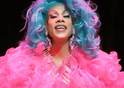 Pepper smiling while wearing a pink fluffy top and light blue wavy wig.