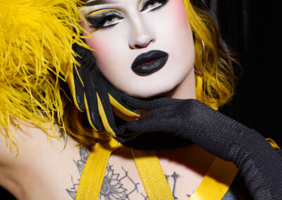 Closeup of Van Goth wearing a black and yellow outfit with one yellow feathered opera glove and one black opera glove.