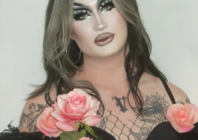 Van Goth wearing a black corset with feather sleeves holding pink roses.