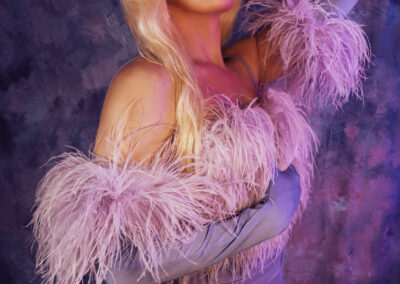 Vanity Affair posing demurely and wearing a light purple dress with feather accents.