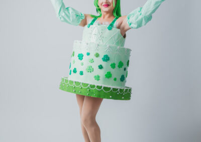Zara Matrix wearing a mint green birthday cake costume and neon green wig, posing with her arms up.