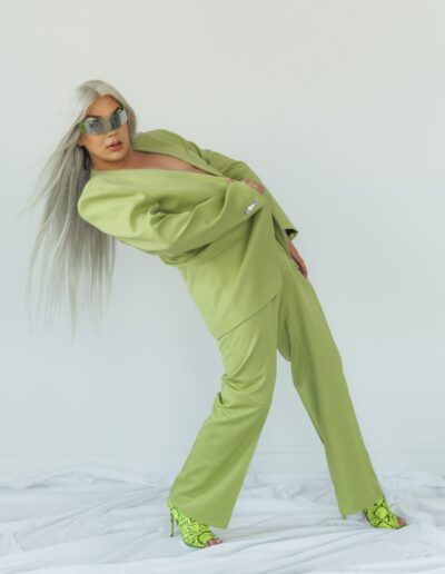 Chelazon Leroux in a green jacket and reflective single-lensed sunglasses, leaning back dramatically while she stares into the camera.