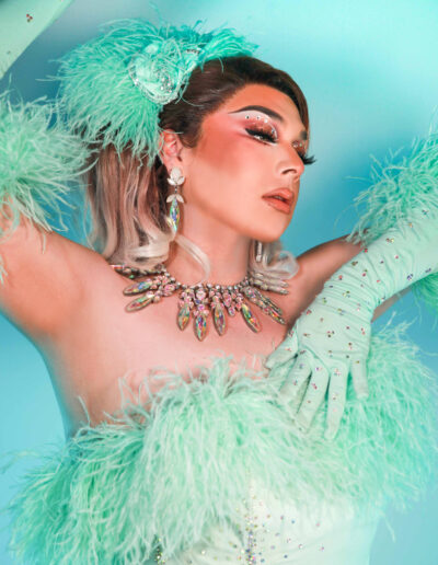 Bust-up view of Chelazon Leroux in a mint feathery outfit posing with her arms up and gazing gently to her left.