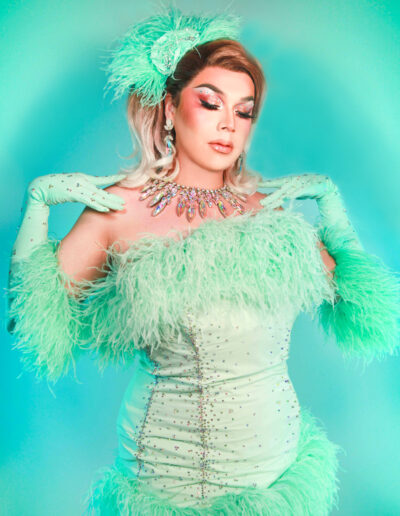 Hips-up view of Chelazon Leroux in a mint dress with feather accents, touching her shoulders and gazing down with her eyes closed.