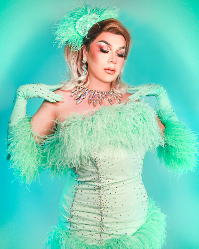 Hips-up view of Chelazon Leroux in a mint dress with feather accents, touching her shoulders and gazing down with her eyes closed.