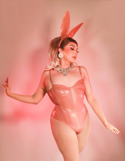 Chelazon Leroux in a peach bunny bodysuit with matching ears and tail, posing demurely while she gazes to her left.