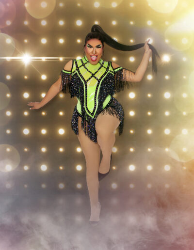 Dulce posing in a neon green and black flapper-style dress, holding her hair and lifting her left knee as if to hop.