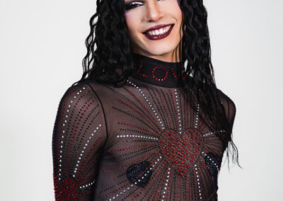 Bust up view of Liquorice in a sheer rhinestoned body suit over a black underbust corset, smiling at the camera.