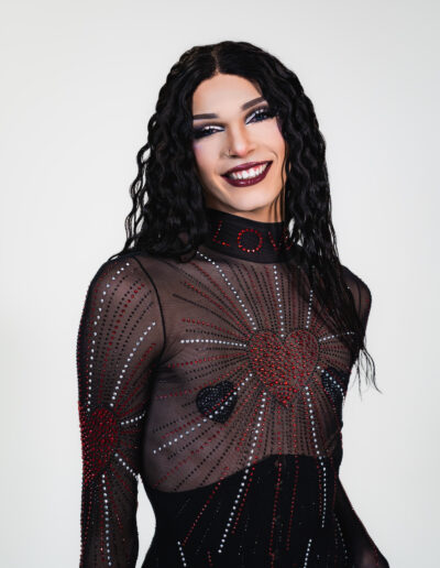 Bust up view of Liquorice in a sheer rhinestoned body suit over a black underbust corset, smiling at the camera.