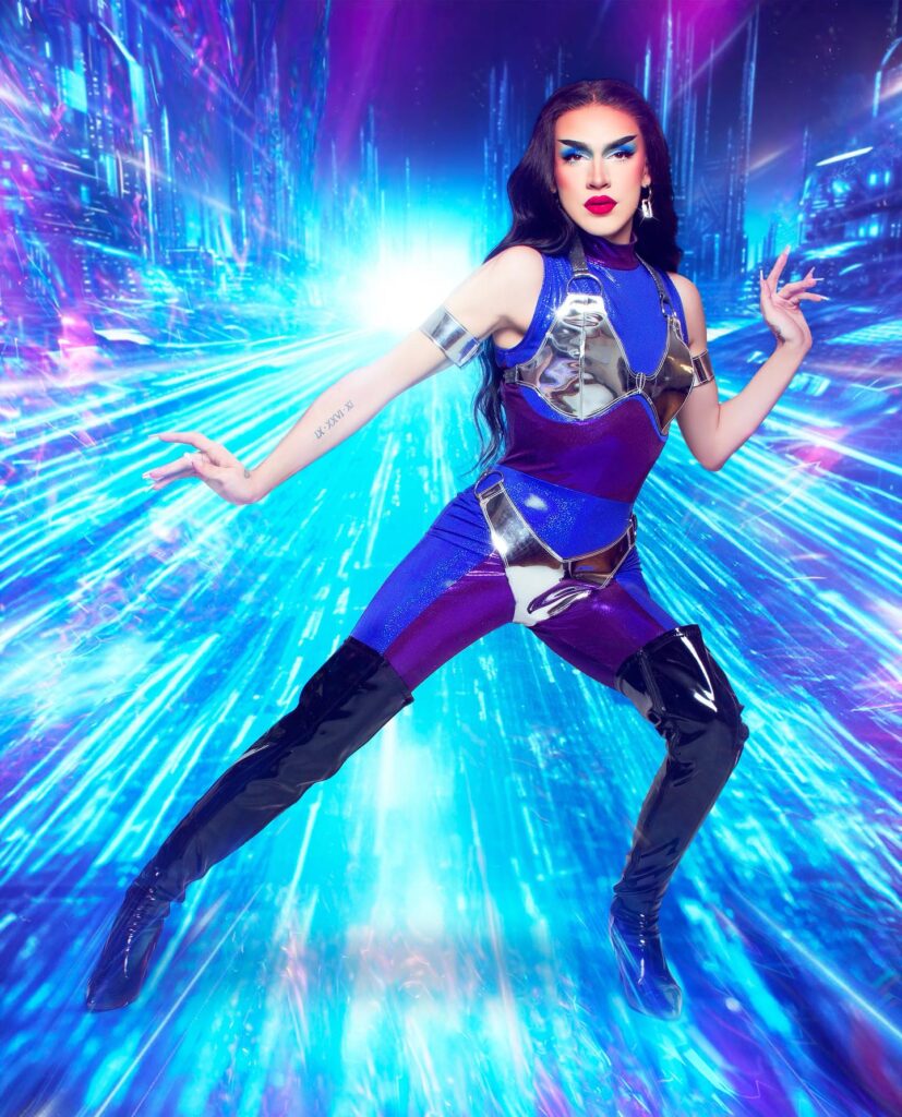 Nicki Nastasia wearing a blue, purple, and silver superhero-looking uniform, posing dramatically.