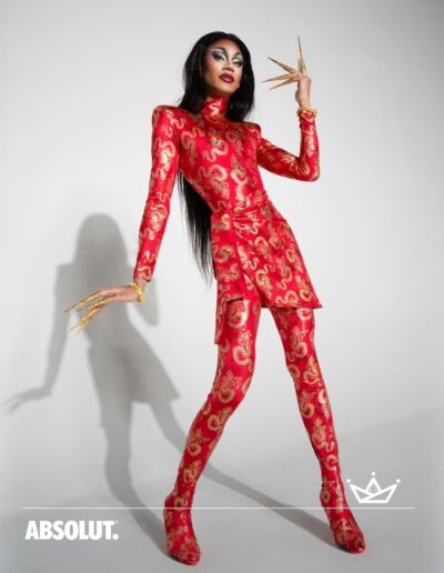 Phoenix Black in a red and gold patterned suit, posing dramatically in a promotional photo for Absolut Empire's Ball.