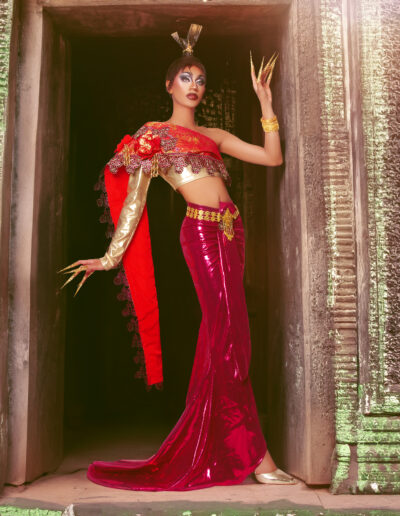 Phoenix Black wearing a red and gold two-piece outfit, Posing in a doorway with her left forearm against the door frame.