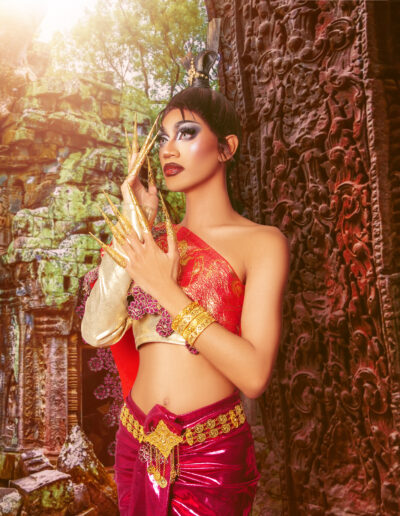 Phoenix Black wearing a red and gold two-piece outfit, posing against a wall with her hands raised towards her face.