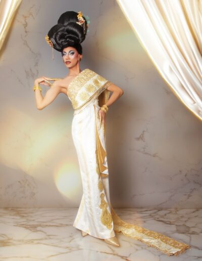 Phoenix Black wearing a white and gold silk gown, posing like a statue with her left hand on her hip and right hand touching her shoulder.