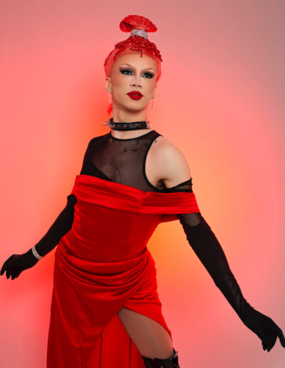 Rosie in a red silk dress over a black sheer tank top with matching black opera gloves, posing dramatically.