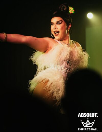 Star performing, pointing at an audience member off camera, in a white rhinestone and feather corset.