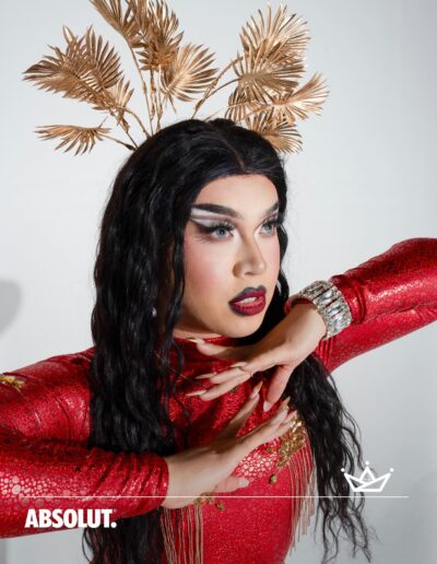 Bust up photo of Star wearing a shimmery red bodysuit with a gold leaf headdress, posing dramatically.