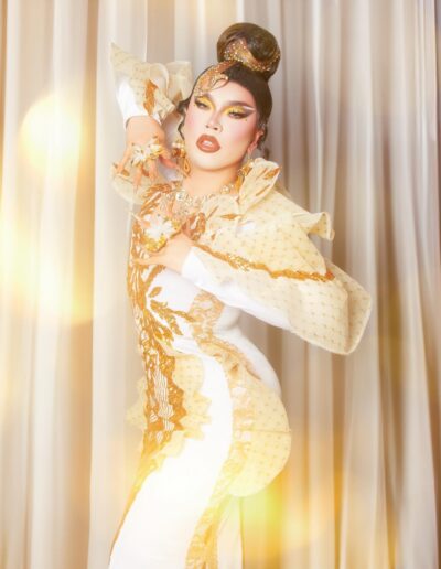 Star posing dramatically with her hands on her chest, wearing a white and gold embellished gown.