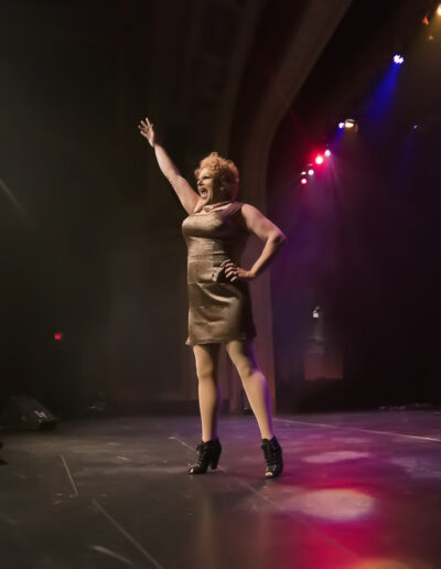 Geena Hayze performing on stage in a shimmery champagne mini dress.