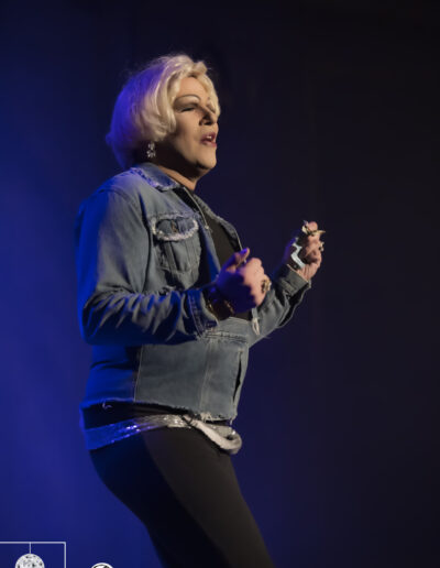 Geena Hayze performing in a denim jacket and mini skirt over a black tank top and leggings.