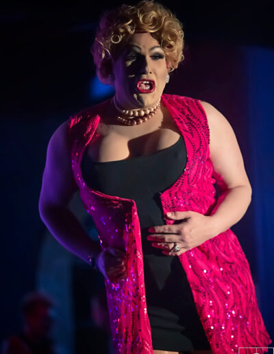 Geena Hayze performing in a pink and black dress with pink rhinestone embellishments.