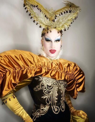 Lua wearing a dark corset with gold embroidery and shiny bronze puffy sleeves, topped with an elaborate gold headdress with black bead accents.