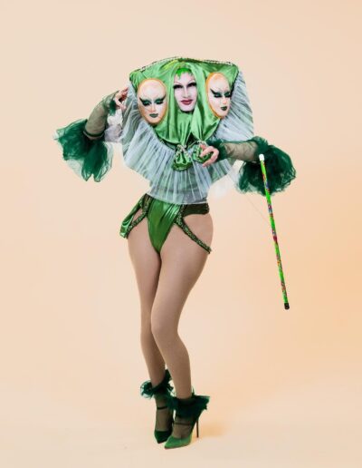 Lua in a green bodysuit with frilly sleeves, a white ruffle collar and a three-faced headdress in green silk.