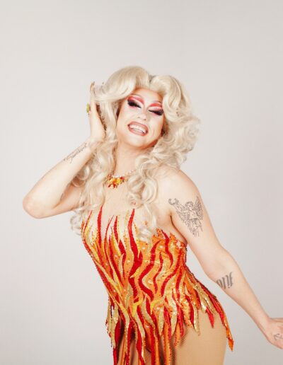 Sunshine Glitterchild wearing a red, orange, and yellow flame outfit, posing flirtatiously.