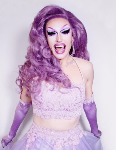 Sunshine Glitterchild smiling while wearing a lavender two piece outfit with violet opera gloves.