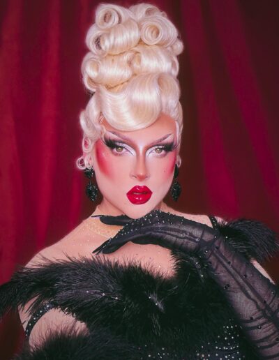 Zsa Zsa wearing a black rhinestone and feathers dress with matching black sheer opera gloves. Her hand is gently resting under her chin.