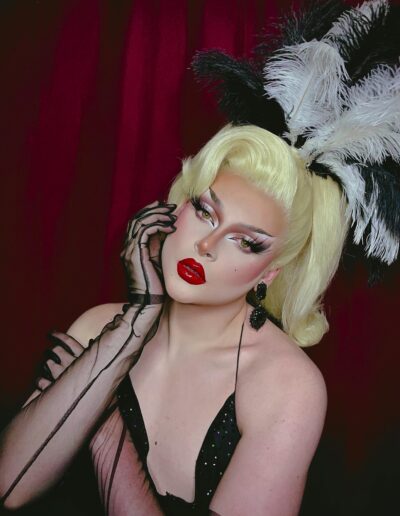 Zsa Zsa wearing a black showgirl outfit, a small black and white feather headpiece, and sheer black opera gloves.