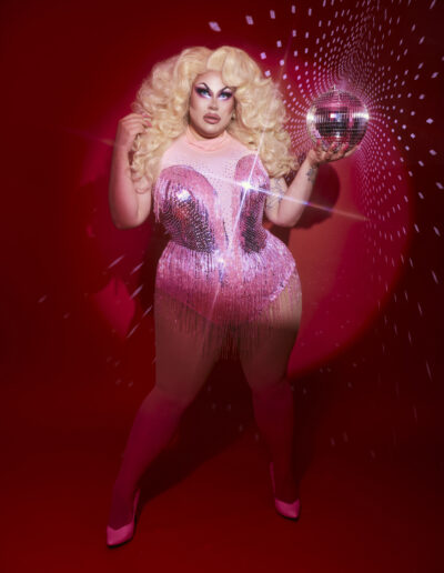 Beth wearing a pink rhinestoned bodysuit, hodling a disco ball.