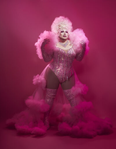 Beth wearing a pink dress with iridescent rhinestones on the bodice and sleeves with ruffled shoulders and skirt, standing proudly.