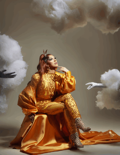 Mya Foxx in a gold bodysuit and robe, sitting and posing contemplatively.