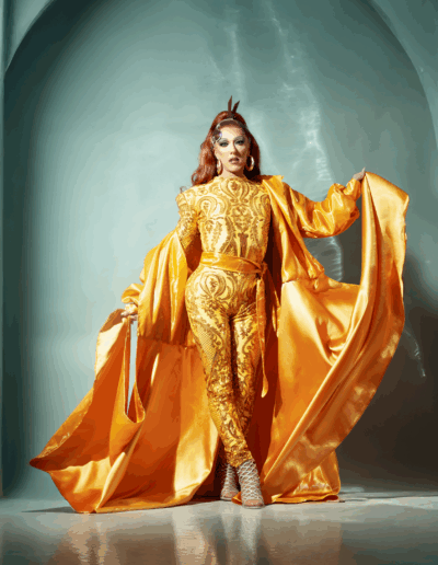 Mya Foxx in a gold bodysuit and robe, posing regally.