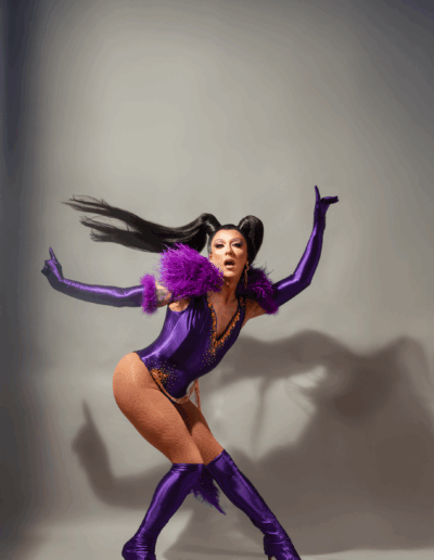 Mya Foxx striking a dramatic pose in a purple bodysuit with matching gloves and boots.