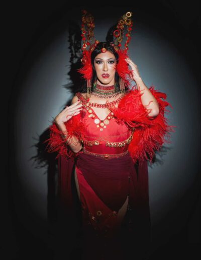 Mya Foxx in a bright red outfit with feather accents, posing dramatically.