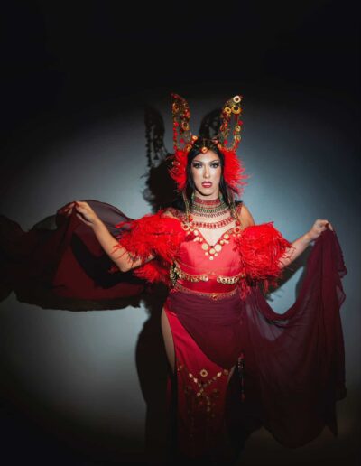 Mya Foxx in a bright red outfit with feather accents, posing with her arms open.