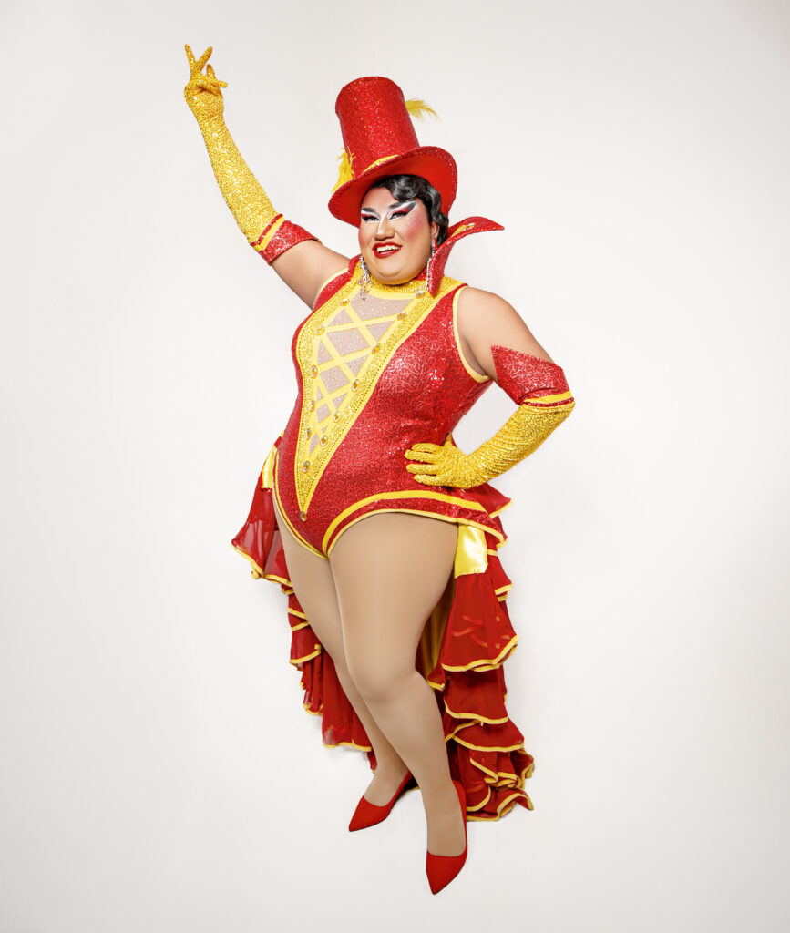 Dulce wearing a bright red and yellow Ringmaster bodysuit with a red stovepipe hat and yellow gloves.